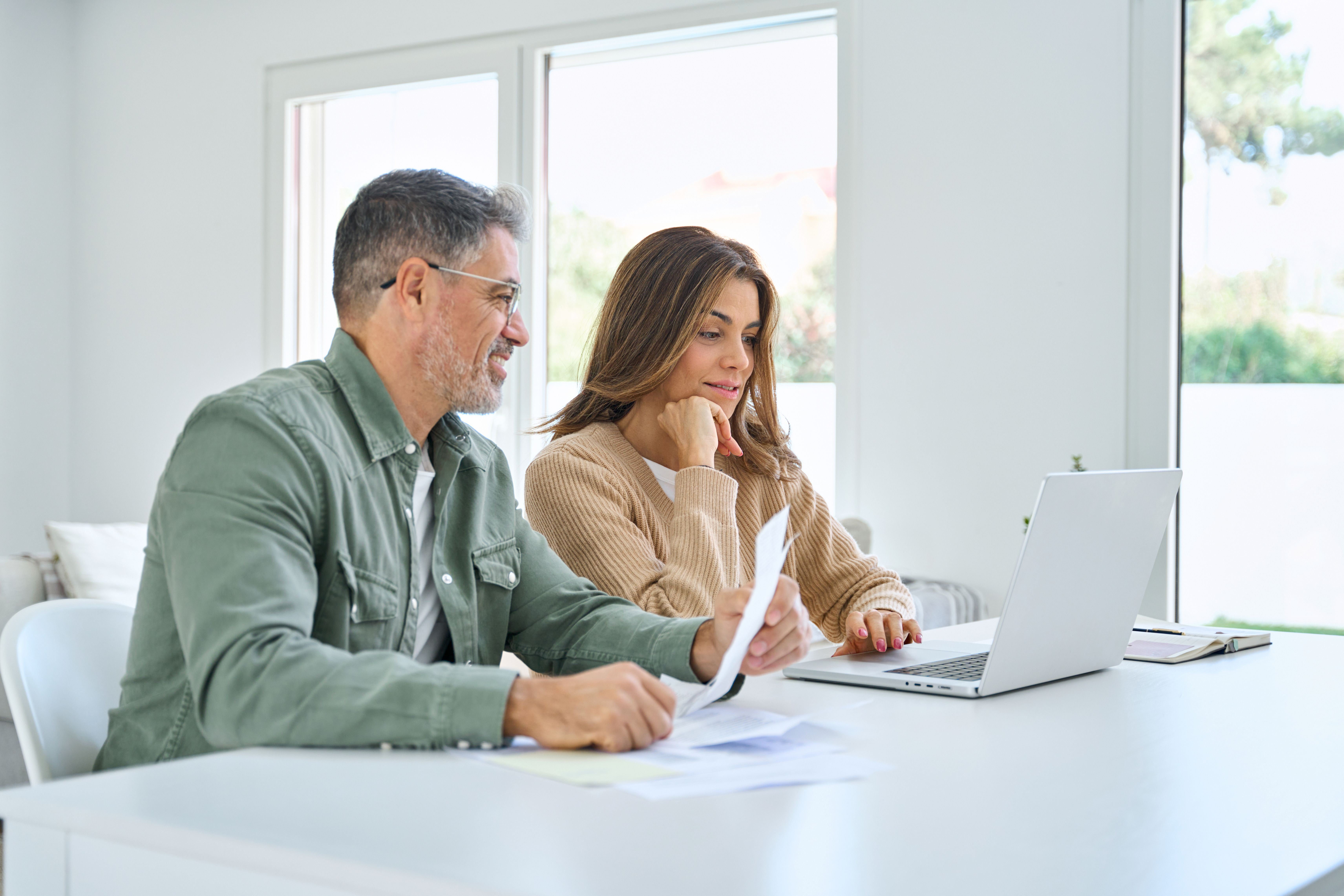 happy middle aged couple deciding on RV rental vs buying by sitting in front of laptop and going though finances